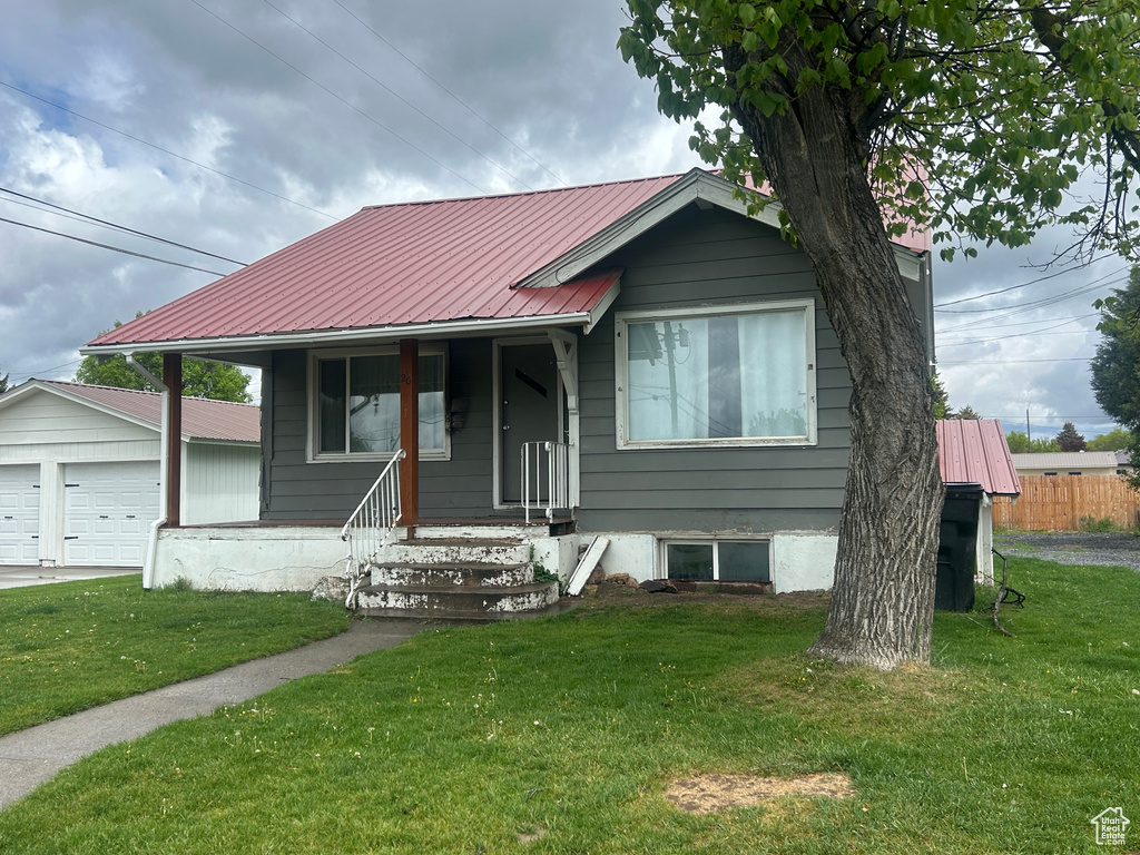 View of front of property with a detached garage, a front yard, metal roof, and an outbuilding