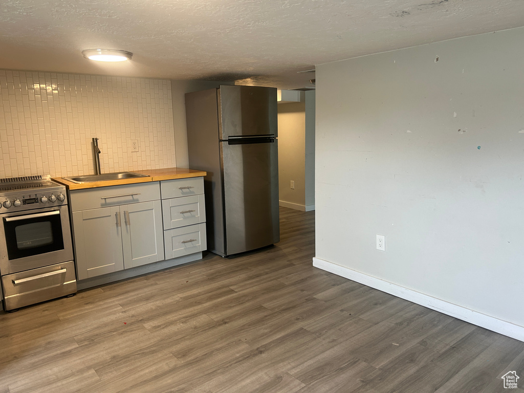 Kitchen featuring appliances with stainless steel finishes, a sink, wood finished floors, a textured ceiling, and baseboards