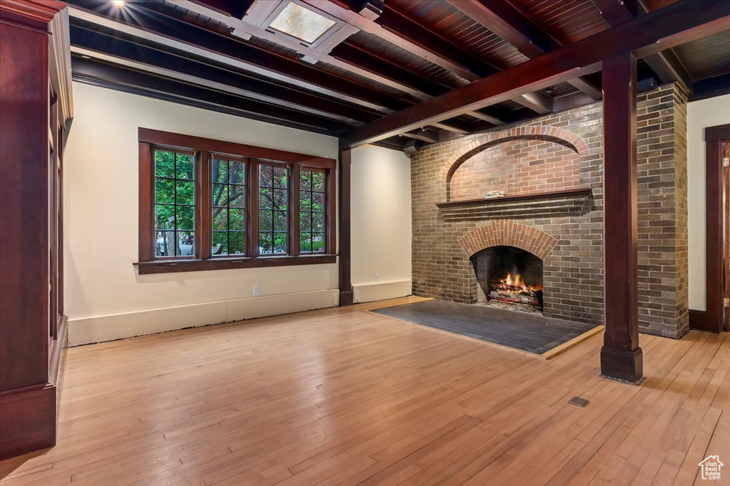 Unfurnished living room with beamed ceiling, wood-type flooring, a fireplace, and baseboards