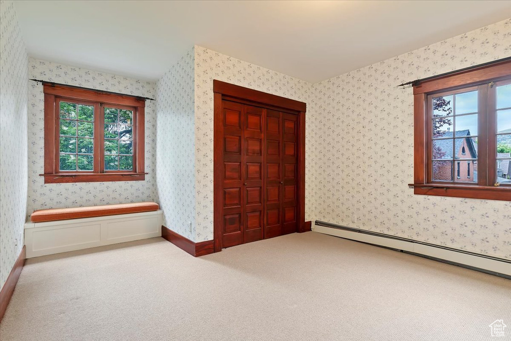 Unfurnished bedroom with multiple windows, wallpapered walls, a baseboard heating unit, carpet, and a closet