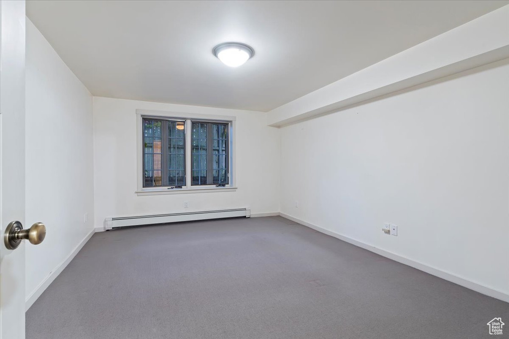 Empty room with a baseboard heating unit, carpet, and baseboards