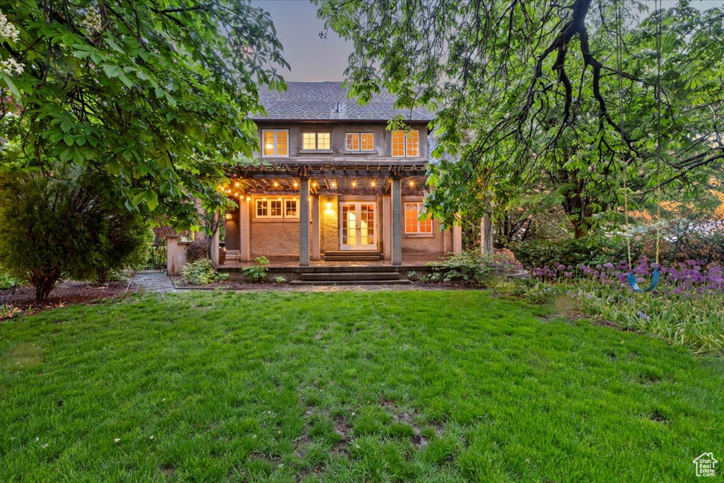 Back of house at dusk featuring a lawn and covered porch