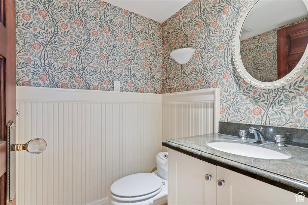 Bathroom with wallpapered walls, toilet, and vanity