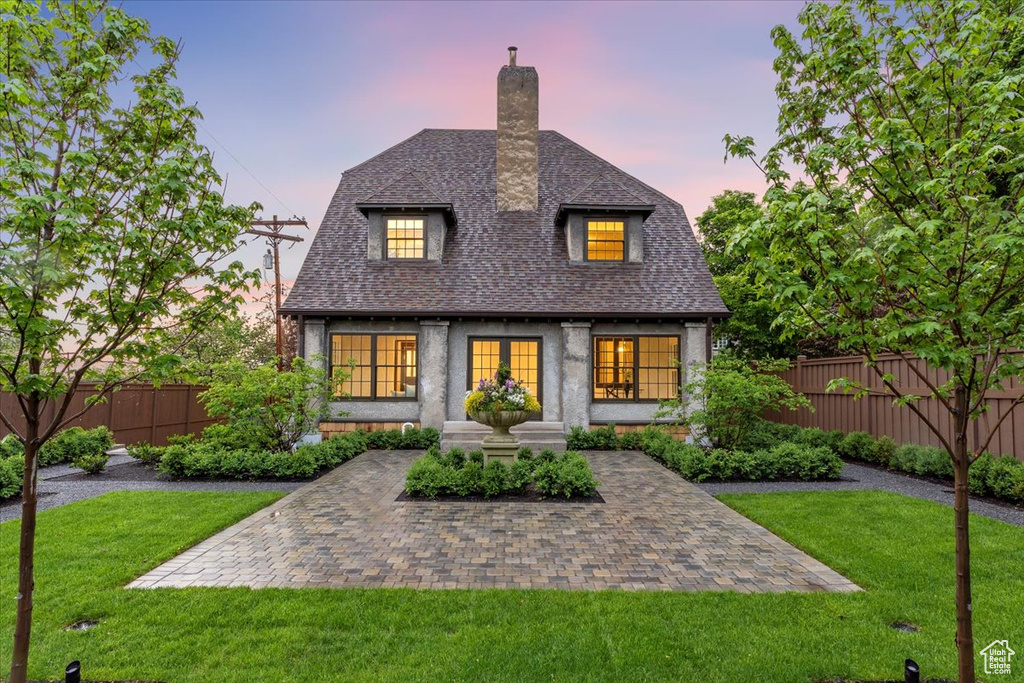 Back of house at dusk with a chimney, roof with shingles, and french doors