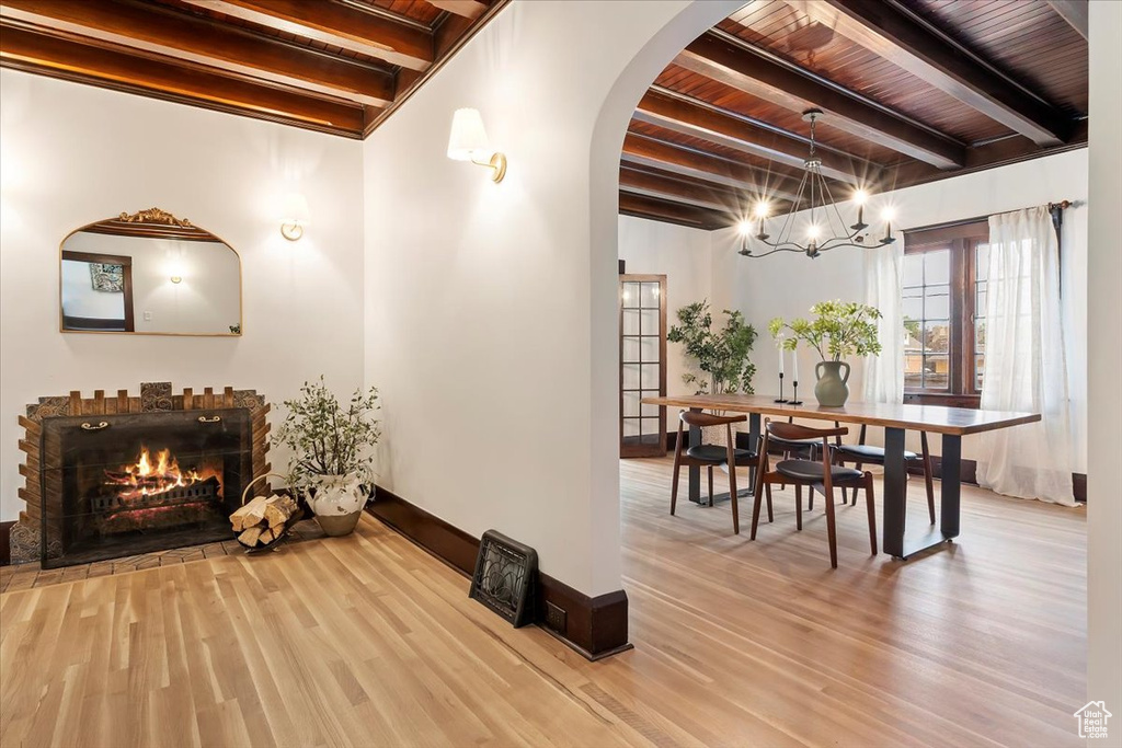 Sitting room featuring beam ceiling, wood finished floors, a chandelier, arched walkways, and a warm lit fireplace