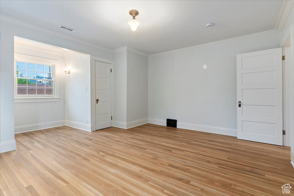 Empty room featuring baseboards, light wood finished floors, crown molding, and a smoke detector