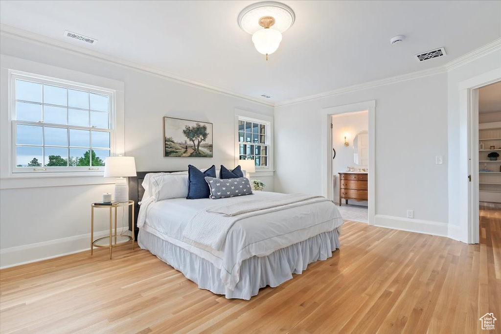 Bedroom with ornamental molding, baseboards, light wood finished floors, and connected bathroom