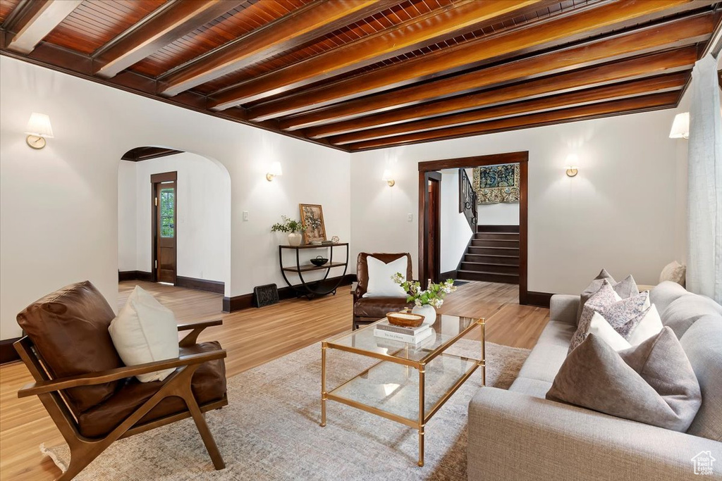 Living room with arched walkways, stairway, beam ceiling, wood finished floors, and baseboards