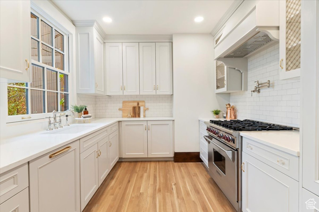 Kitchen featuring stainless steel range, a sink, backsplash, custom range hood, and white cabinets