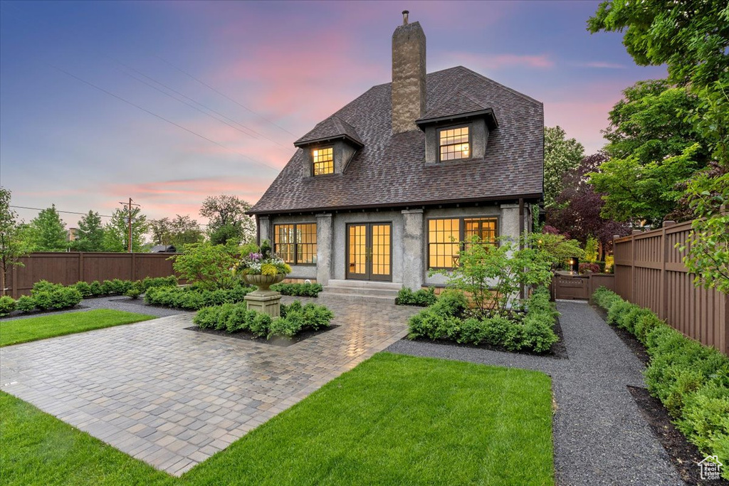 Back of house at dusk with french doors, a chimney, and roof with shingles