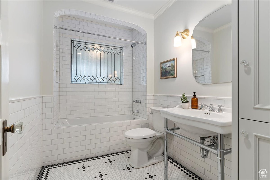 Bathroom featuring toilet, ornamental molding, tile patterned flooring, tile walls, and tiled shower / bath combo