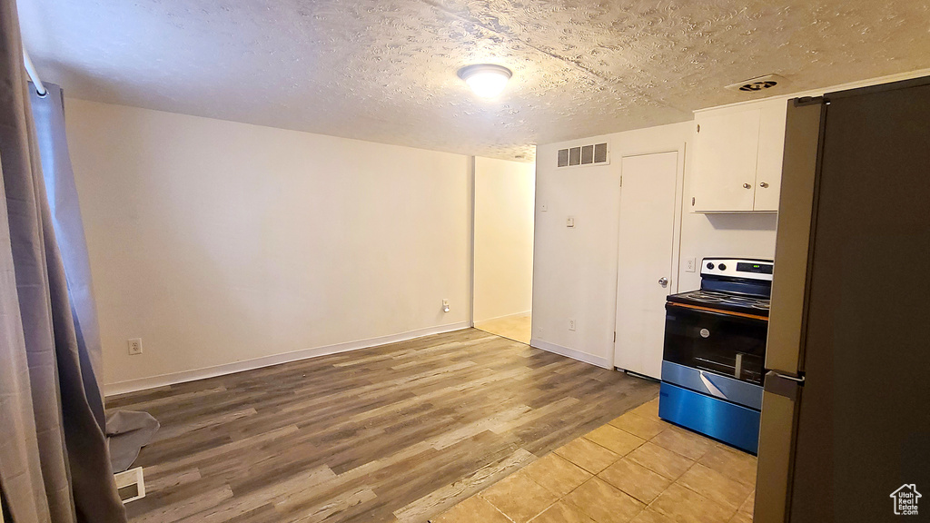 Spare room featuring light wood-style flooring, a textured ceiling, and baseboards