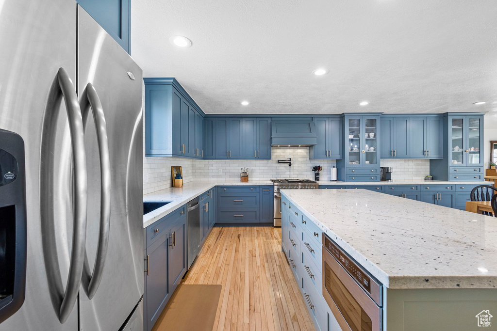 Kitchen featuring appliances with stainless steel finishes, blue cabinetry, decorative backsplash, a center island, and light wood-style flooring