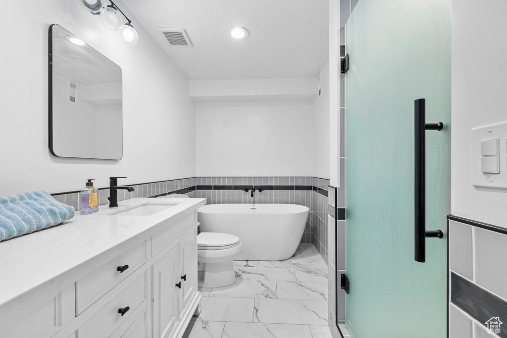 Bathroom with marble finish flooring, a soaking tub, wainscoting, vanity, and toilet