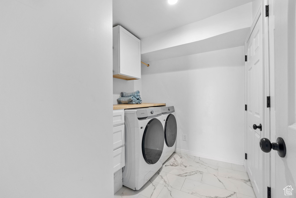 Laundry area with washer and clothes dryer, light marble finish floors, cabinet space, and baseboards