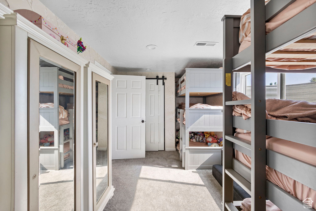Unfurnished bedroom with carpet floors, a barn door, and a textured ceiling