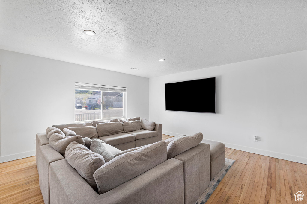 Living area featuring a textured ceiling, baseboards, wood finished floors, and recessed lighting