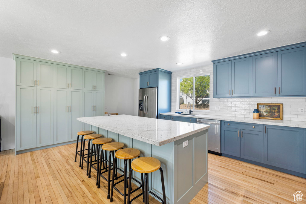 Kitchen featuring appliances with stainless steel finishes, blue cabinetry, a sink, a kitchen island, and tasteful backsplash