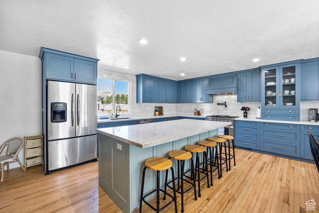 Kitchen featuring appliances with stainless steel finishes, blue cabinetry, custom range hood, a sink, and a kitchen island
