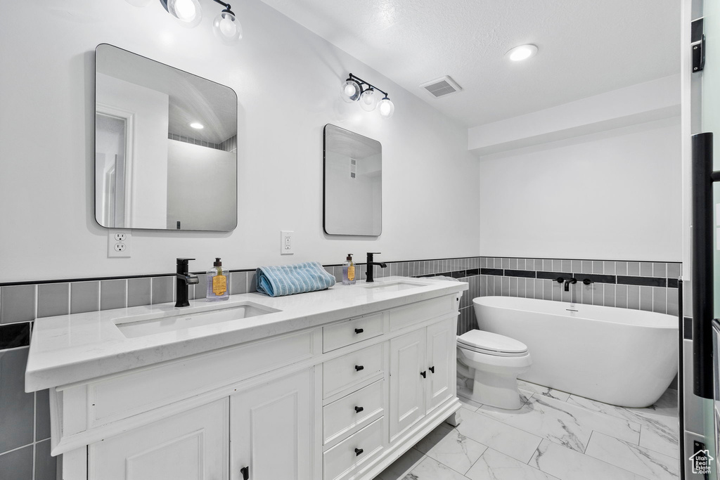 Bathroom featuring marble look tile flooring, a soaking tub, double vanity, a wainscoted wall, and tile walls