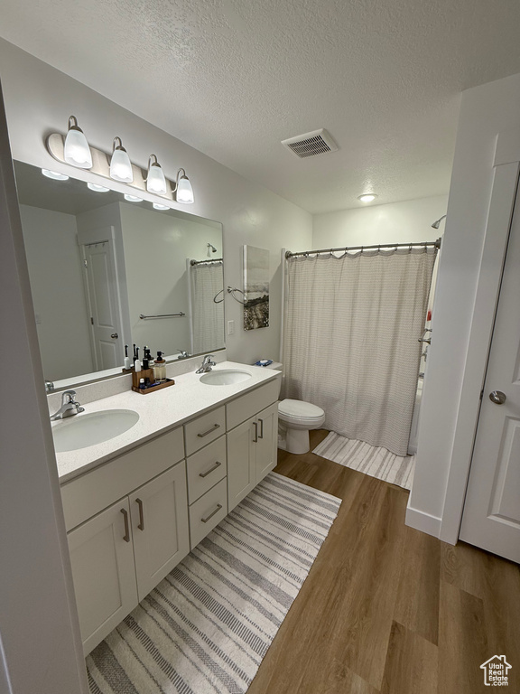 Full bath featuring wood finished floors, toilet, a textured ceiling, double vanity, and a shower with shower curtain