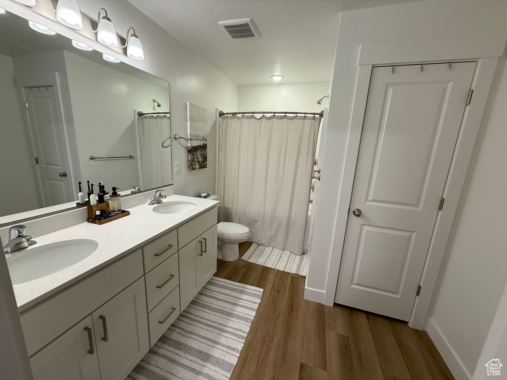 Bathroom with wood finished floors, toilet, double vanity, and baseboards