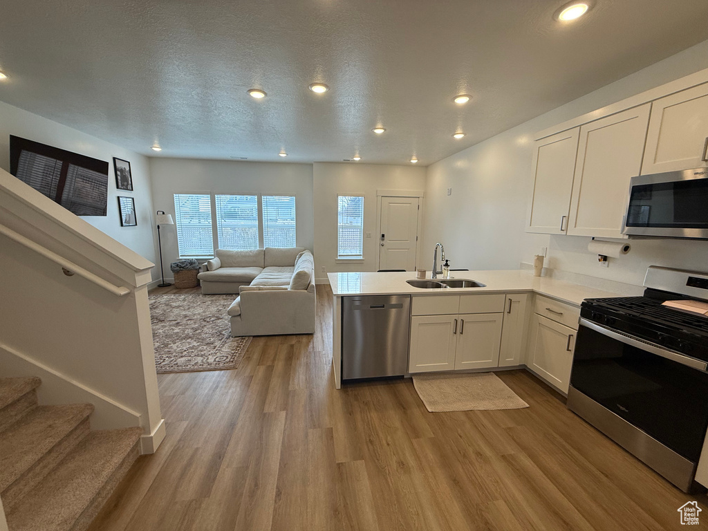 Kitchen featuring stainless steel appliances, a sink, a peninsula, white cabinetry, and open floor plan