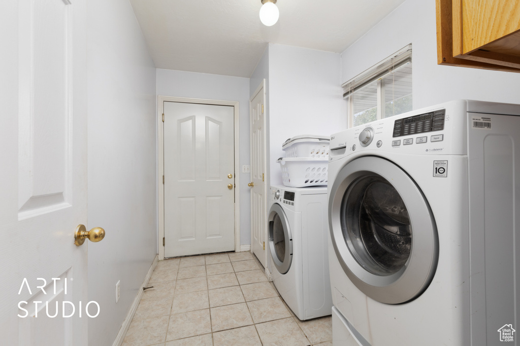 Washroom featuring washing machine and clothes dryer, light tile patterned floors, baseboards, and cabinet space