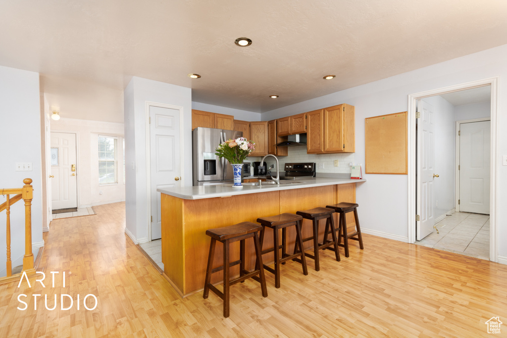 Kitchen featuring stainless steel appliances, under cabinet range hood, a peninsula, light wood finished floors, and backsplash