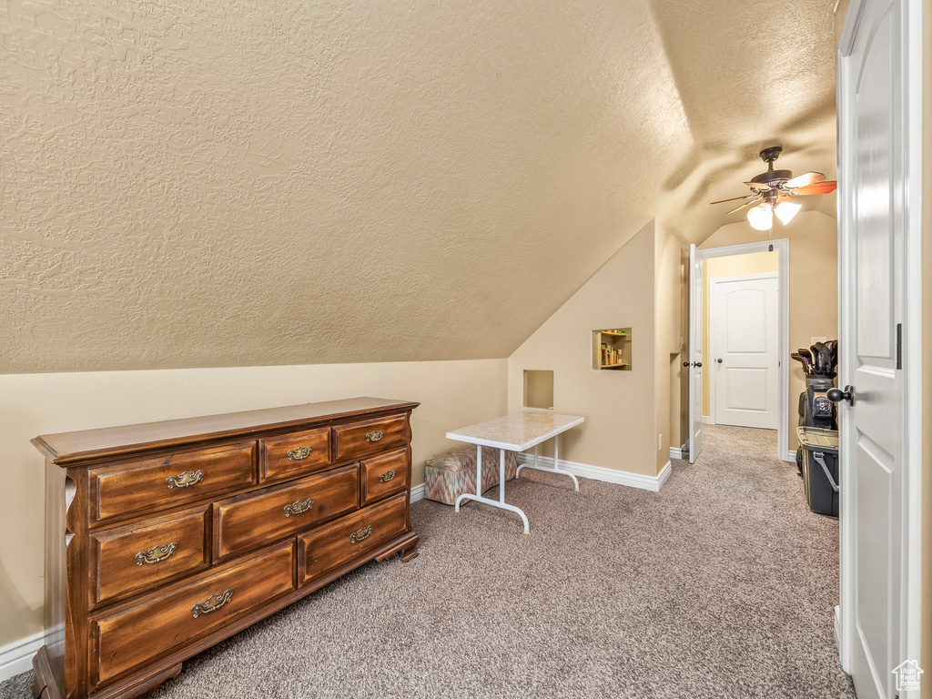 Carpeted bedroom featuring a textured ceiling, vaulted ceiling, baseboards, and a ceiling fan
