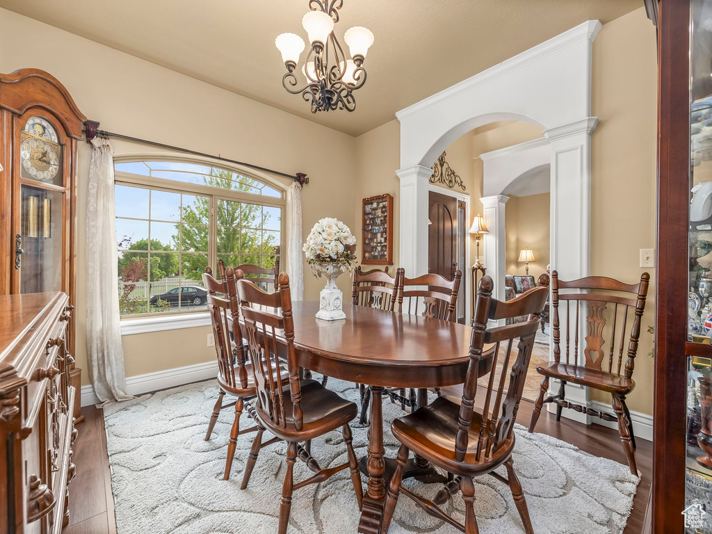 Dining area with ornate columns, arched walkways, baseboards, a chandelier, and wood finished floors