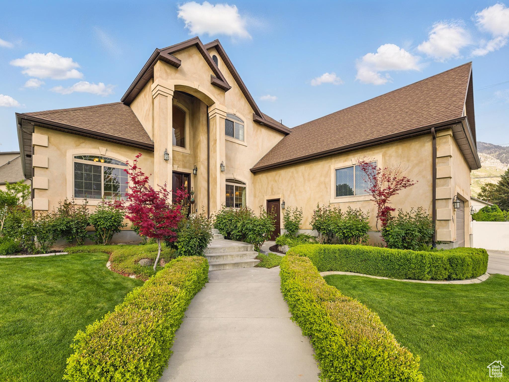 View of front facade featuring stucco siding, a front lawn, and a shingled roof