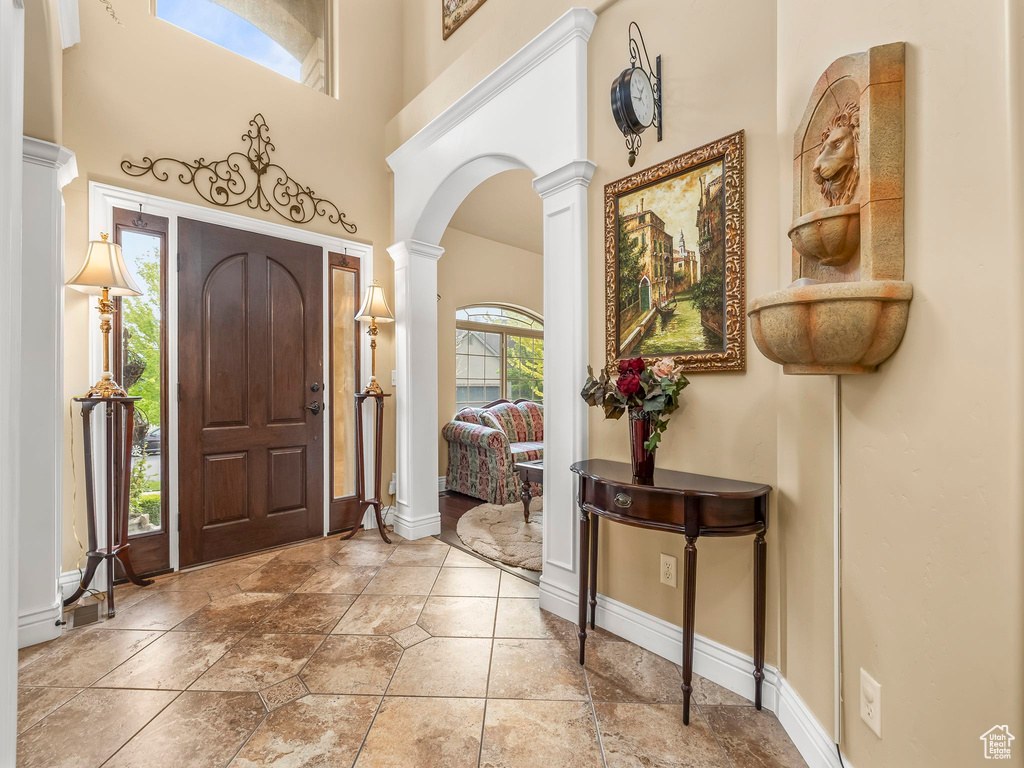 Entrance foyer with decorative columns, baseboards, a towering ceiling, arched walkways, and stone tile flooring
