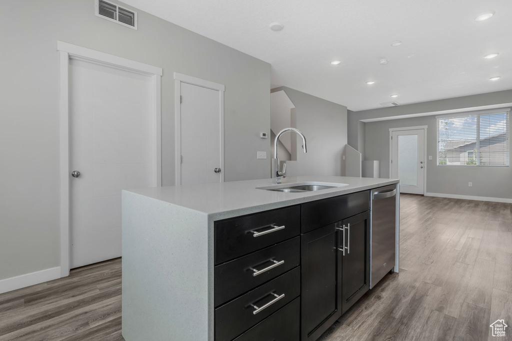 Kitchen featuring a sink, light wood finished floors, stainless steel dishwasher, light countertops, and baseboards