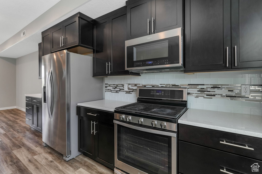 Kitchen with stainless steel appliances, light wood-style flooring, backsplash, and light countertops