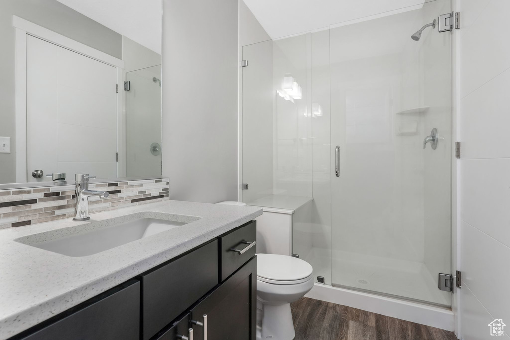 Bathroom with wood finished floors, a stall shower, toilet, and decorative backsplash