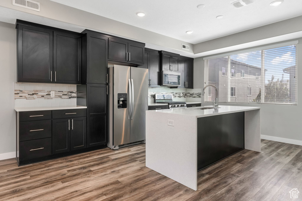 Kitchen featuring stainless steel appliances, a sink, dark cabinets, light countertops, and decorative backsplash
