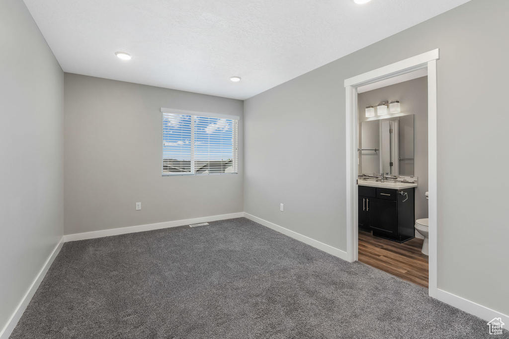 Unfurnished bedroom with dark carpet, baseboards, ensuite bath, and recessed lighting