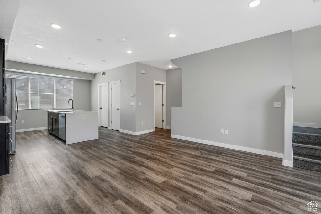 Unfurnished living room featuring a sink, baseboards, dark wood-style flooring, recessed lighting, and stairs