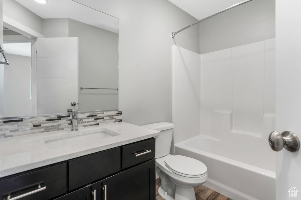 Full bath with decorative backsplash, wood finished floors, toilet, vanity, and shower / bathtub combination