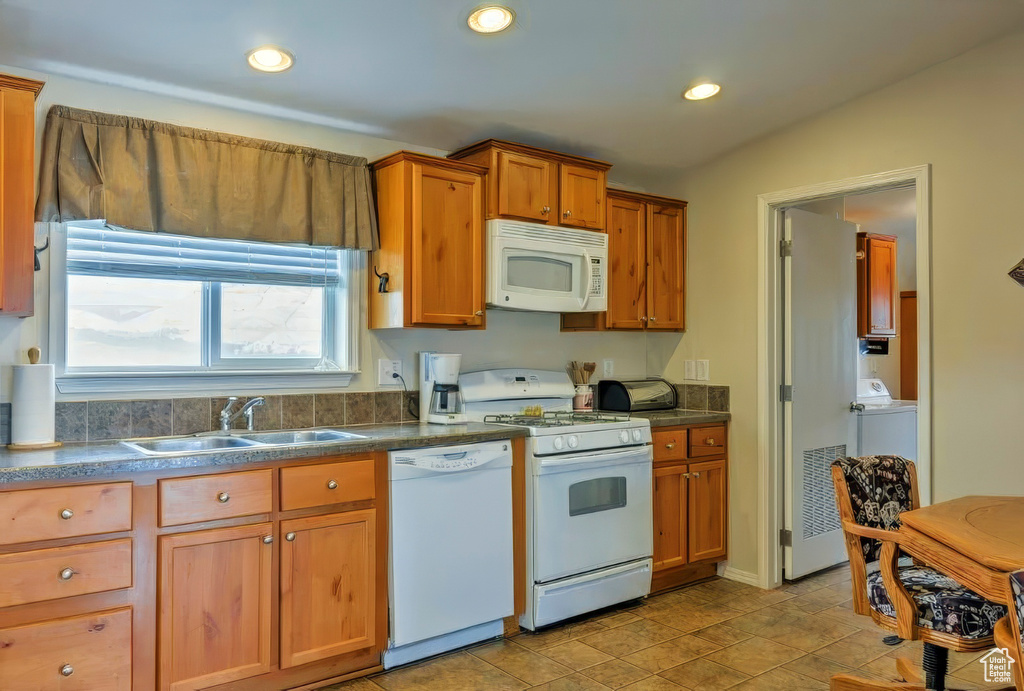 Kitchen featuring a sink, brown cabinetry, white appliances, recessed lighting, and dark countertops