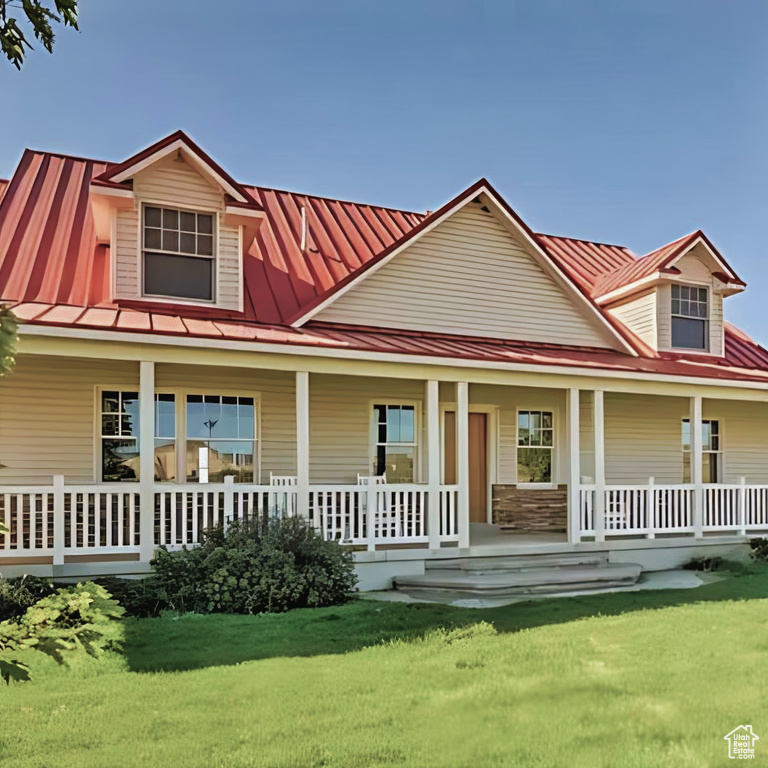 Farmhouse inspired home with covered porch, metal roof, a front yard, and a standing seam roof