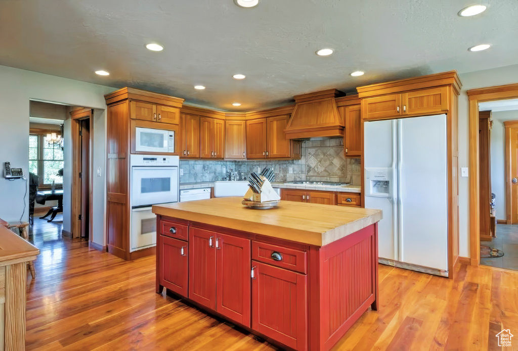 Kitchen featuring premium range hood, white appliances, wood counters, decorative backsplash, and light wood-style floors