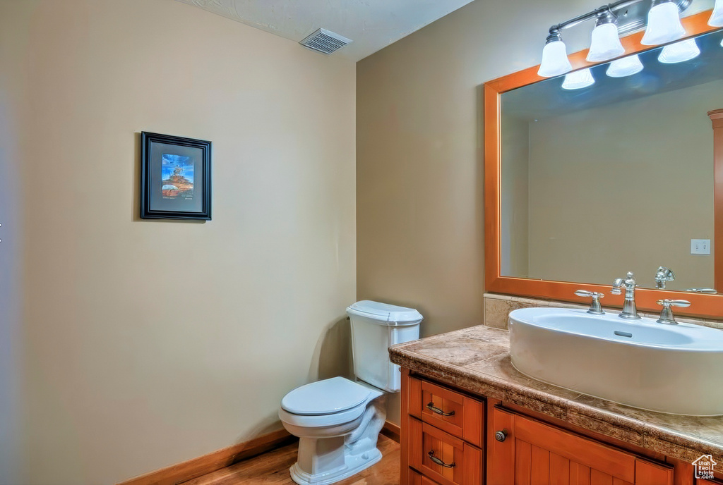 Half bath with toilet, baseboards, visible vents, vanity, and wood finished floors