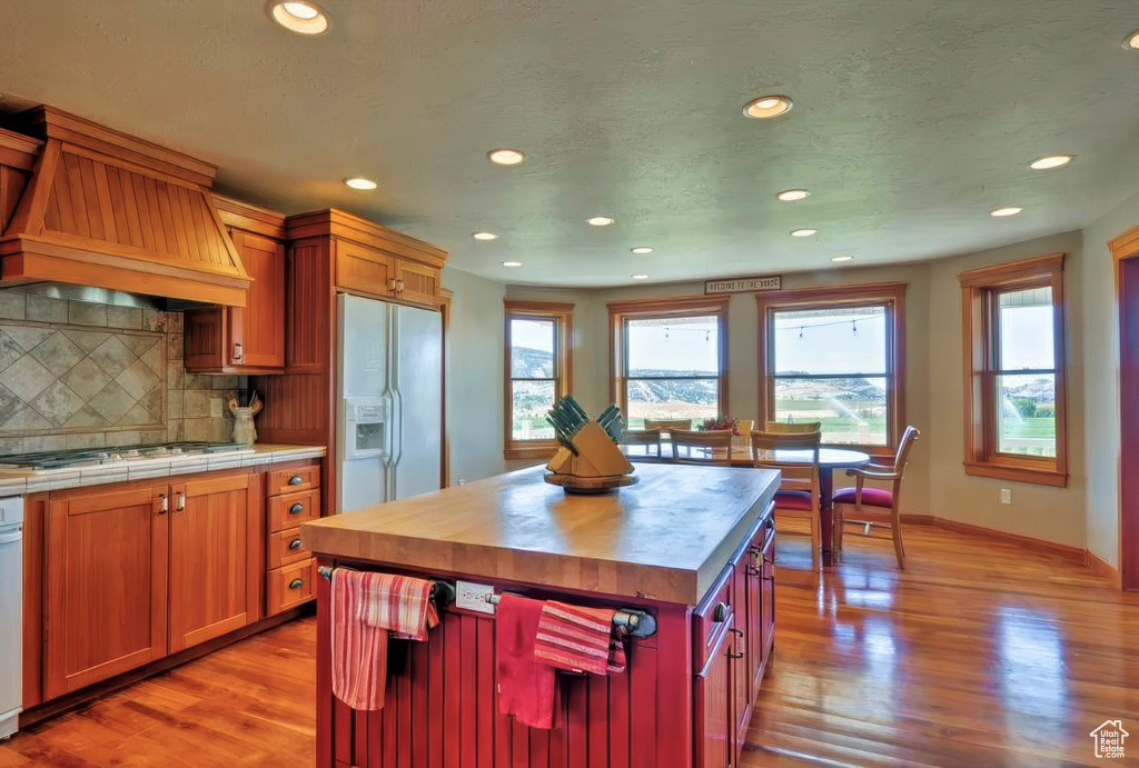 Kitchen featuring white fridge with ice dispenser, recessed lighting, light wood-style flooring, gas stovetop, and custom range hood