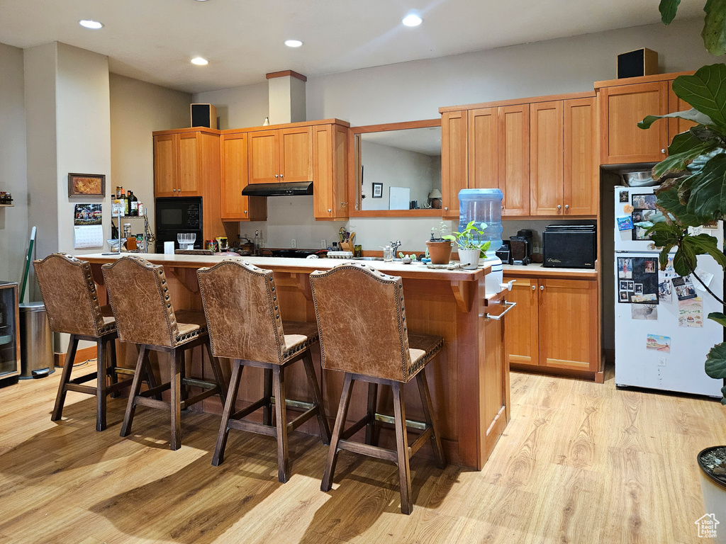 Kitchen featuring freestanding refrigerator, light wood-style floors, under cabinet range hood, a breakfast bar, and recessed lighting