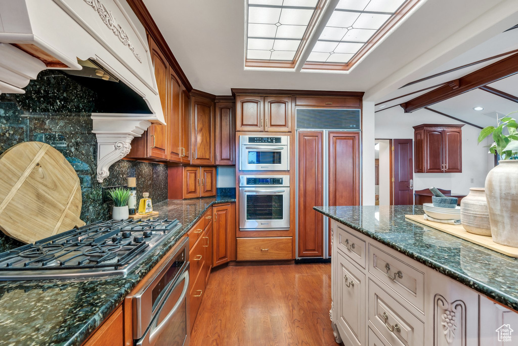 Kitchen featuring paneled built in refrigerator, under cabinet range hood, stainless steel gas cooktop, light wood-style floors, and decorative backsplash