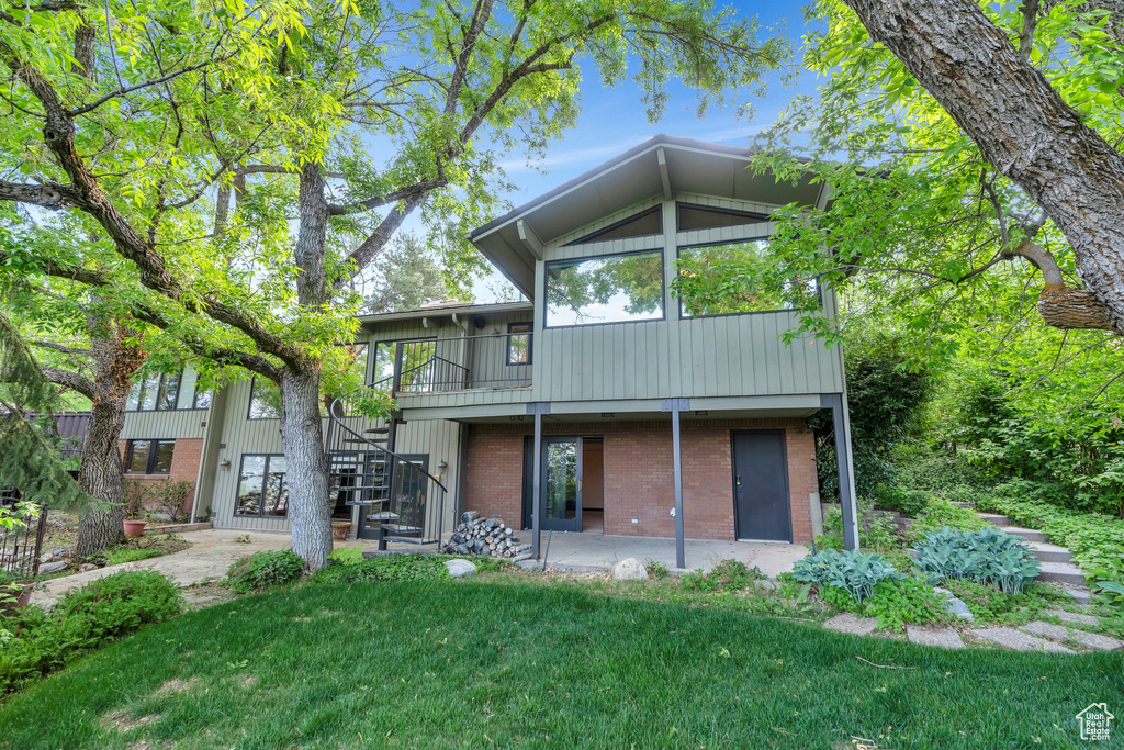 Rear view of property with stairway, brick siding, a lawn, and a patio