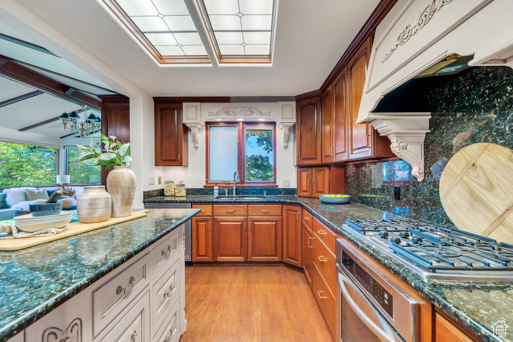 Kitchen with stainless steel appliances, a sink, dark stone countertops, light wood-style flooring, and tasteful backsplash