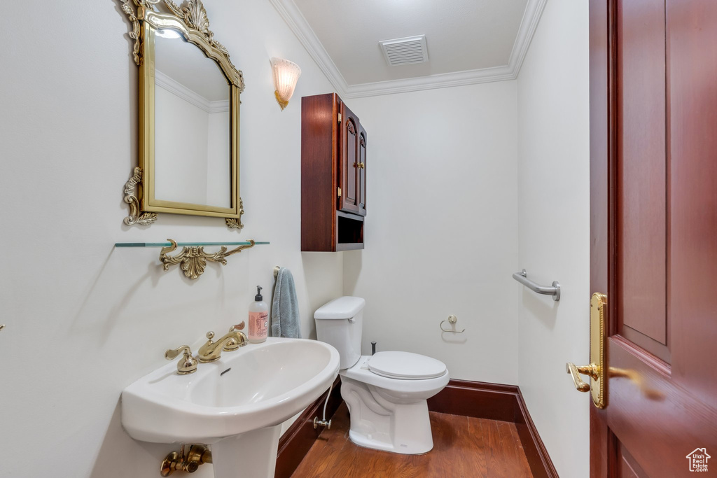 Bathroom featuring wood finished floors, crown molding, toilet, a sink, and baseboards